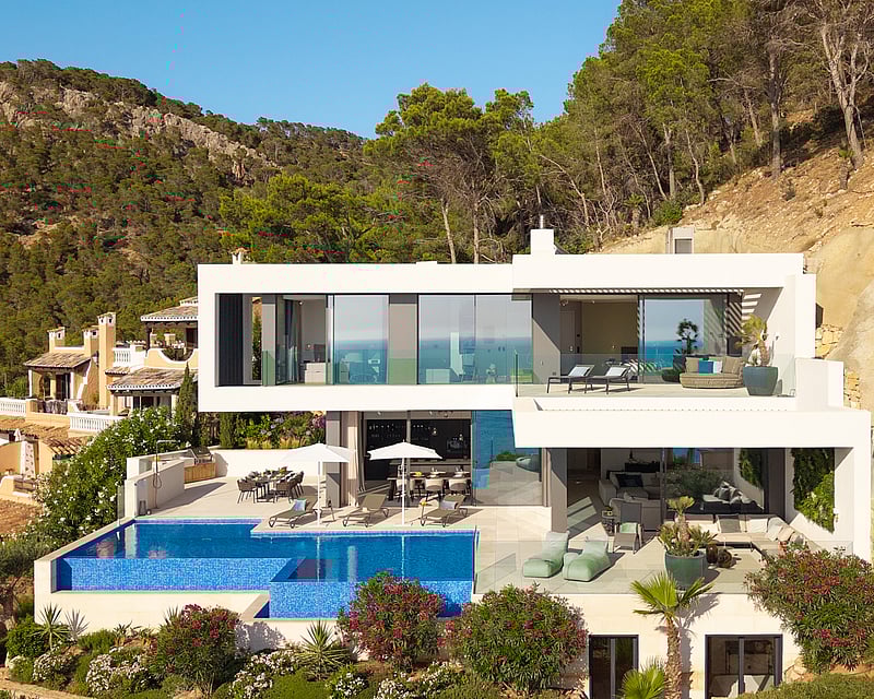 Multi-level modern white villa on a hillside featuring a large infinity pool, lounge terraces, and lush greenery.