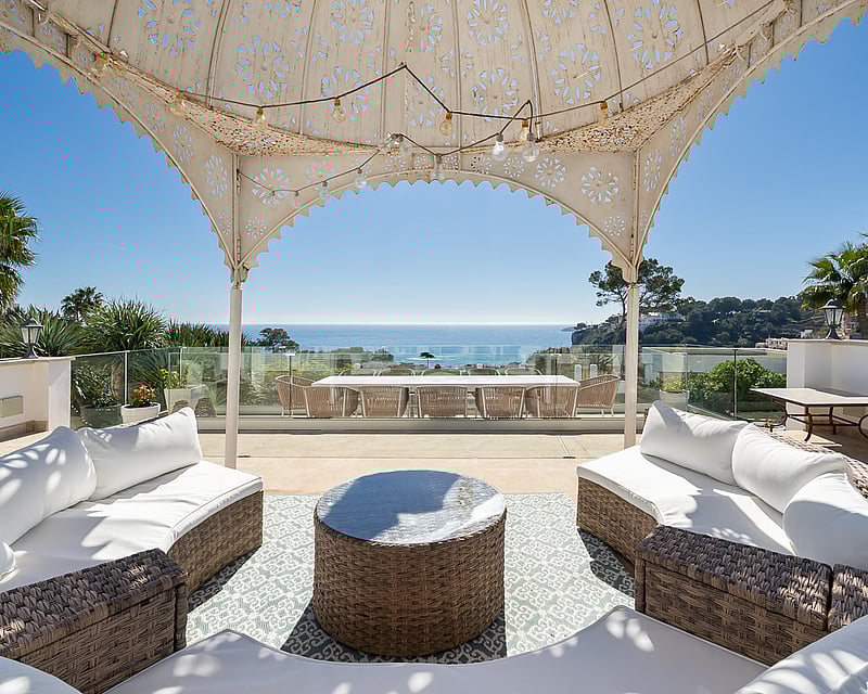 Spacious terrace with wicker sofas under a decorative gazebo overlooking the Mediterranean sea.