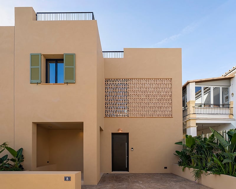Modern sand-colored villa exterior with green shutters, decorative brick screen, and tropical landscaping.