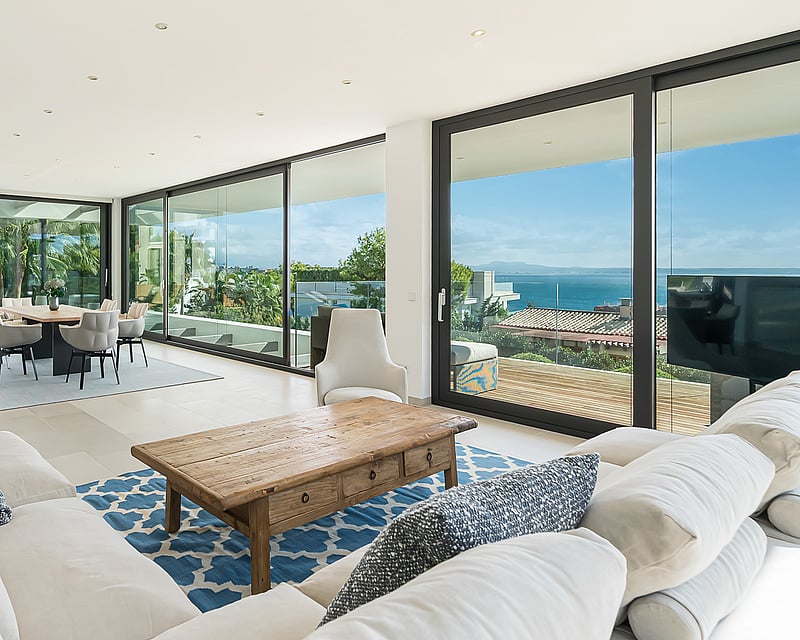 Spacious living room with white sofas, wooden coffee table, and large glass doors opening to a sea-view terrace.