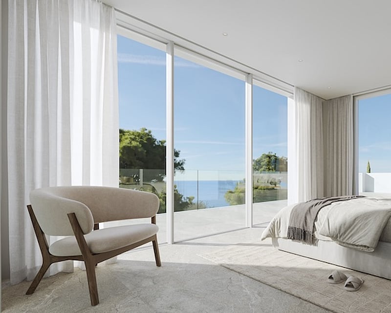 Dormitorio principal minimalista con ventanales de suelo a techo que dan a una terraza de piedra con vistas al Mediterráneo.
