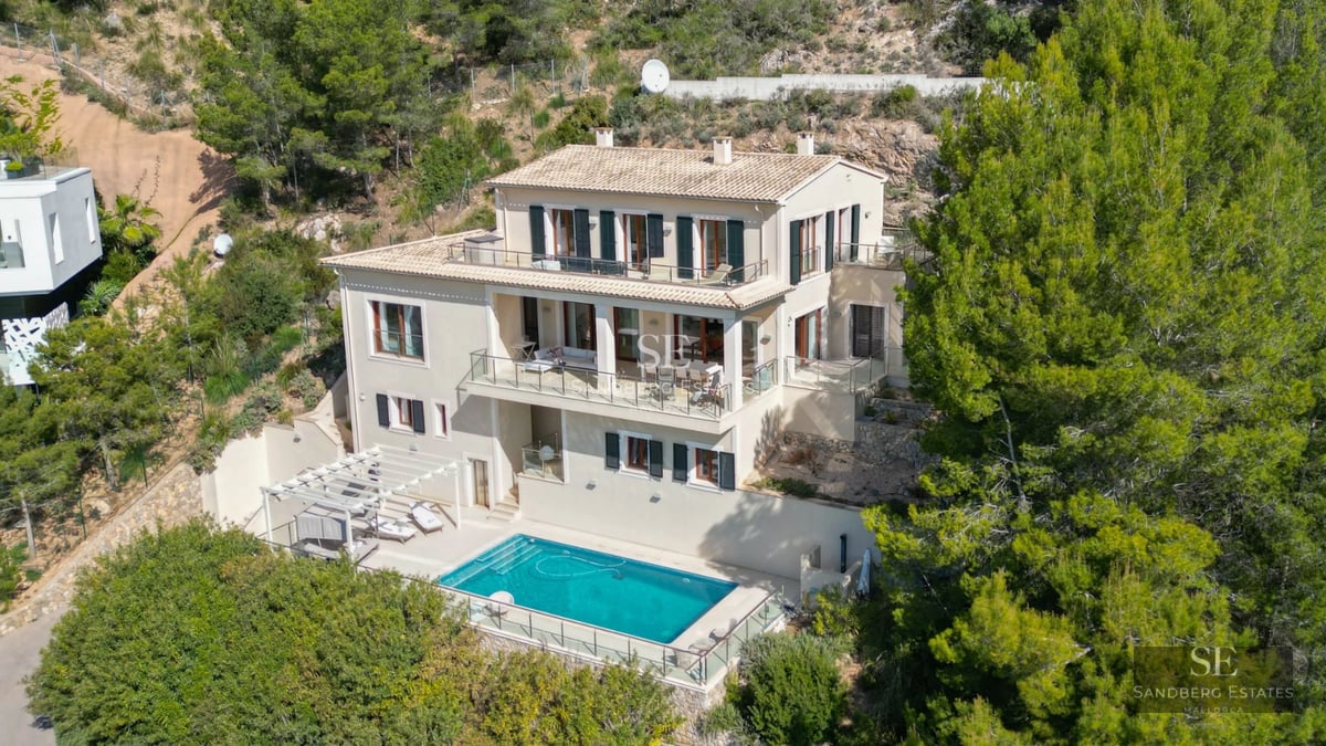 View of a luxurious infinity pool with sea views from a modern villa featuring large windows and a terrace.