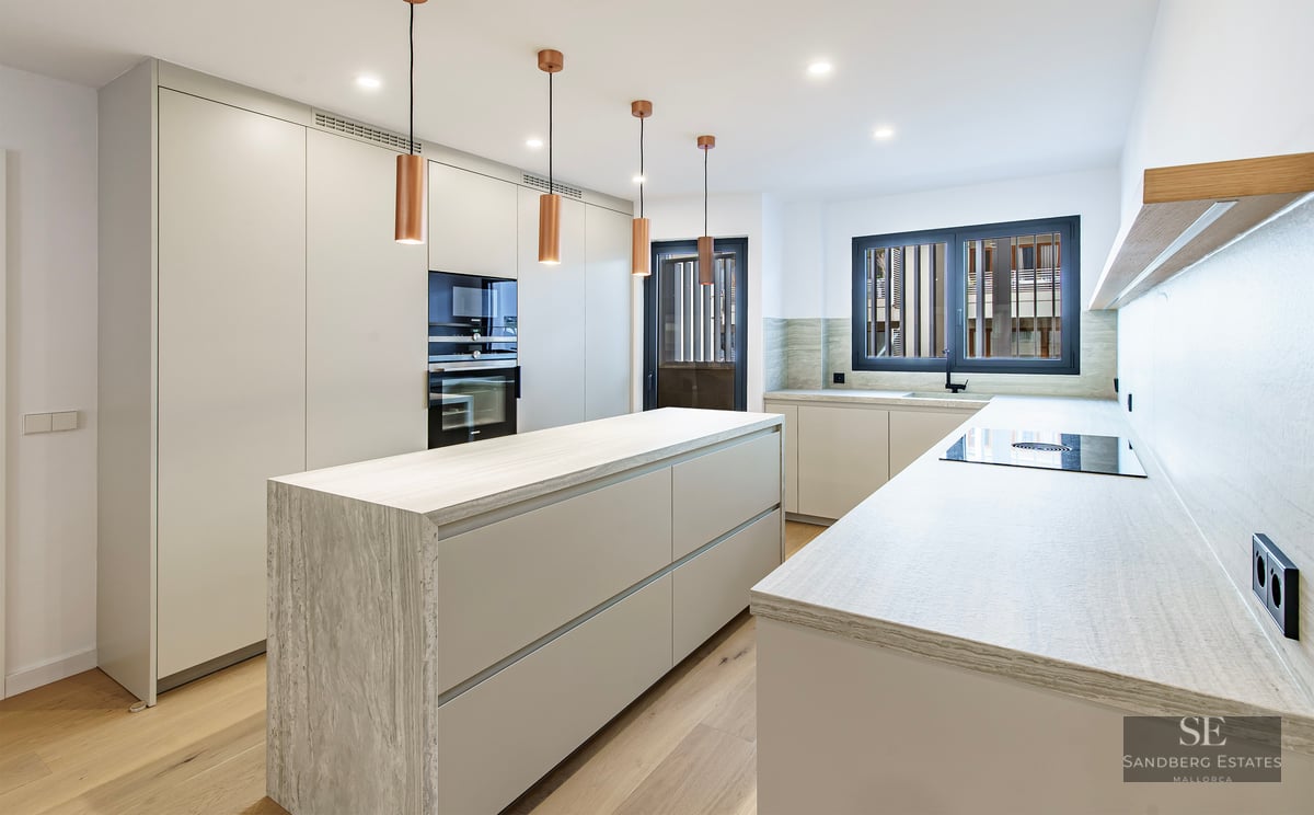 Cuisine contemporaine blanche avec îlot en pierre, suspensions en cuivre et parquet en bois.