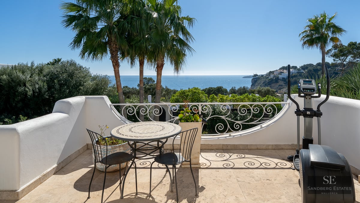White terrace with wrought iron furniture and an elliptical machine overlooking palm trees and the Mediterranean sea.
