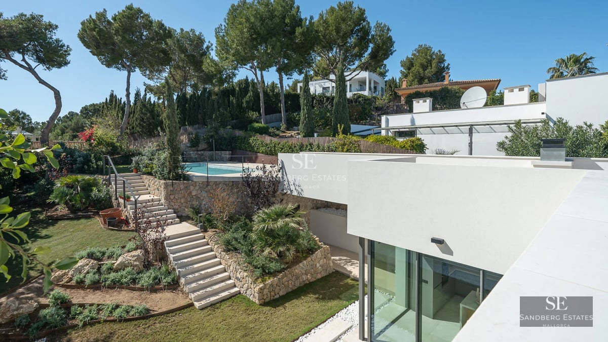 Spacious living room with floor-to-ceiling windows, grey sofa, fireplace, light wood flooring and garden view. Modern and bright design.