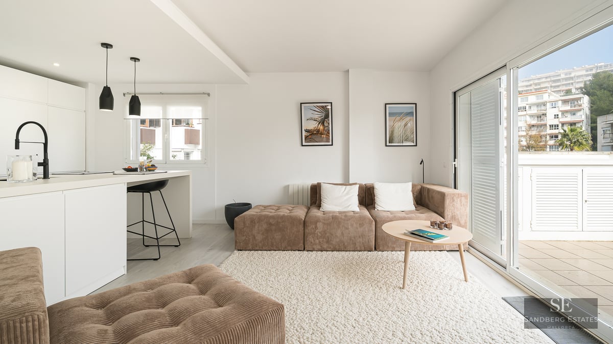 Bright living room with brown corduroy modular sofa, white textured rug, kitchen island, and large glass doors to a balcony.