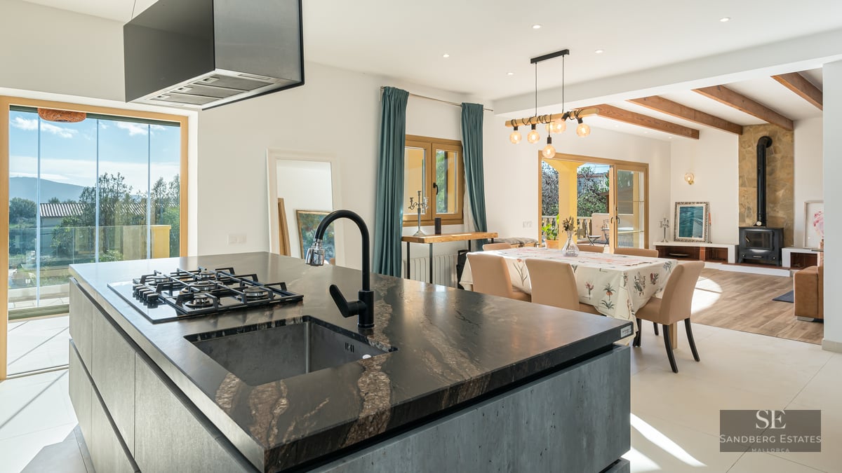 Modern kitchen island with dark stone countertop opening into a dining and living area with a fireplace.