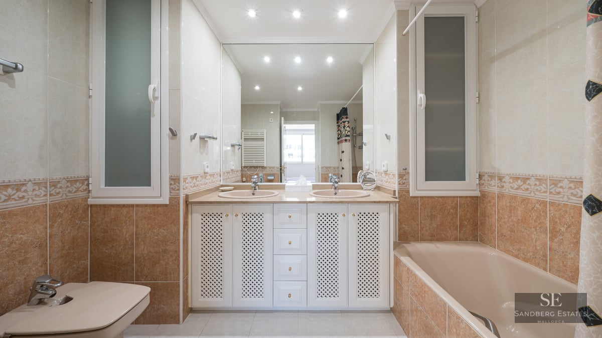 Spacious bathroom with double sinks, large mirror, bathtub, and bidet in warm beige and terracotta tones.