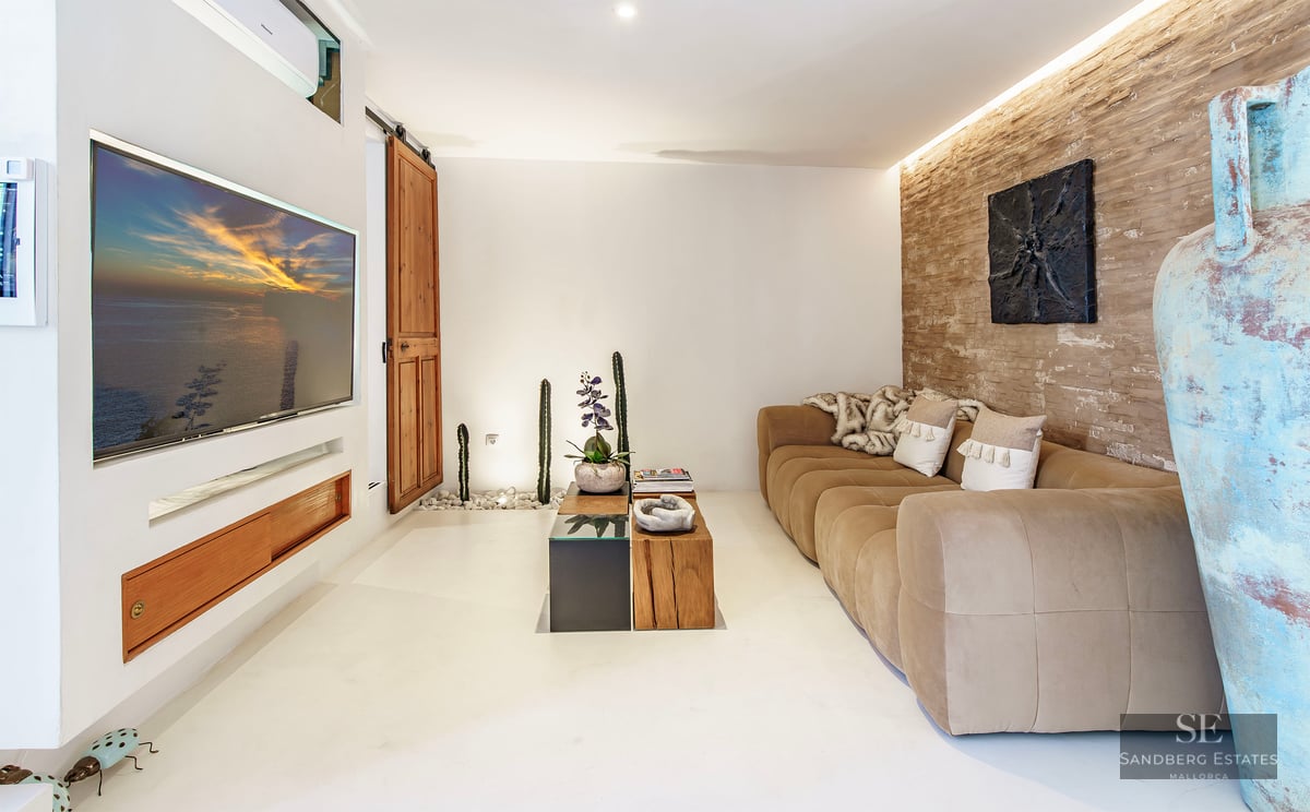 Living room featuring a beige sofa, rustic stone wall, built-in television, and Mediterranean decor elements.