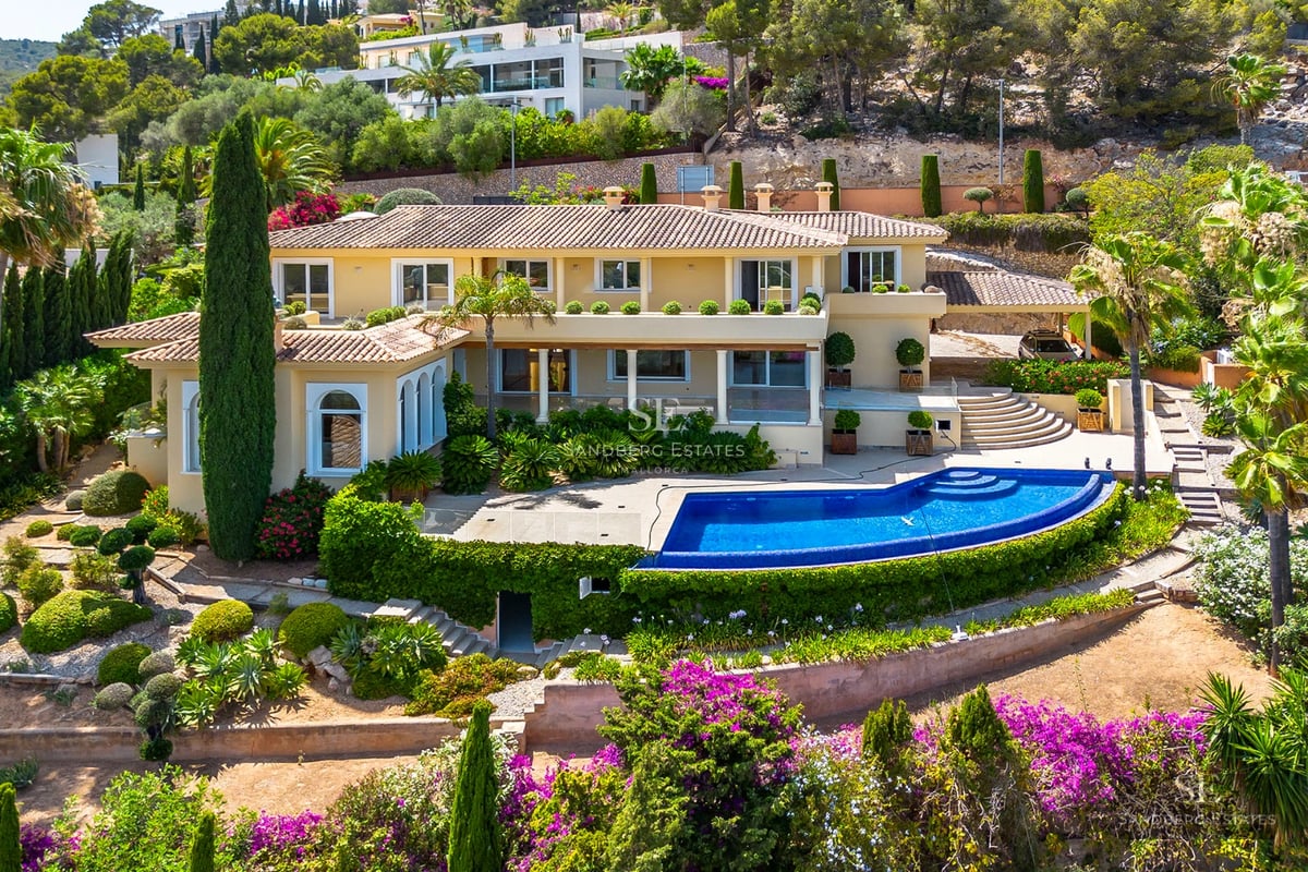 View of a luxury infinity pool with sun loungers and umbrellas, surrounded by a garden and overlooking the sea. Modern and elegant architecture.
