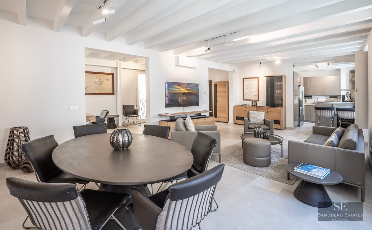 Salon moderne avec table ronde, canapés en cuir, plafond à poutres blanches et télévision murale.