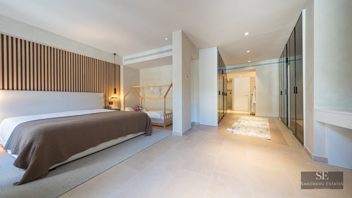 Modern bedroom featuring a wood slat wall, large bed, toddler area, and sleek glass-fronted wardrobes.