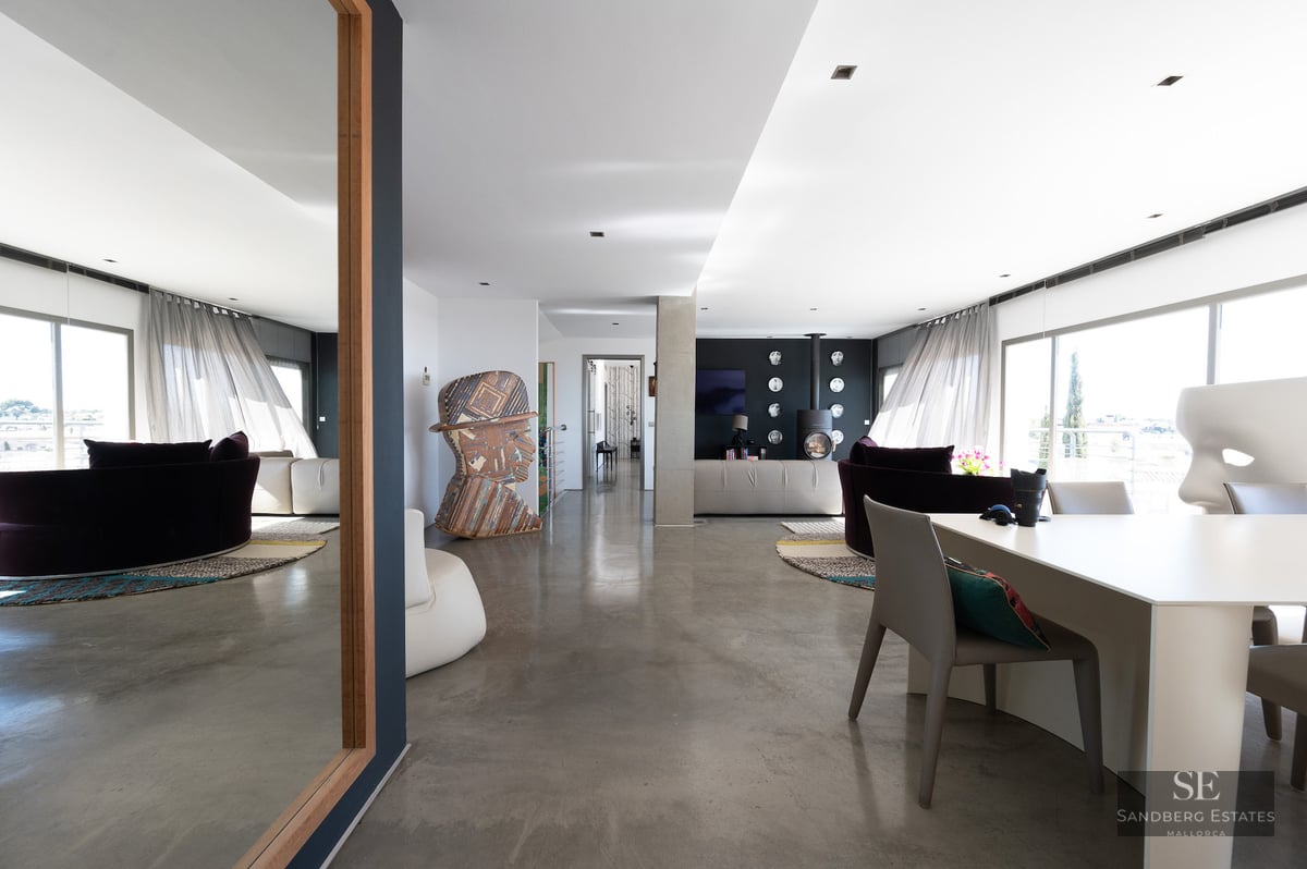 Bright interior with polished concrete floors, a large mirror reflecting a sofa, and contemporary art sculptures.