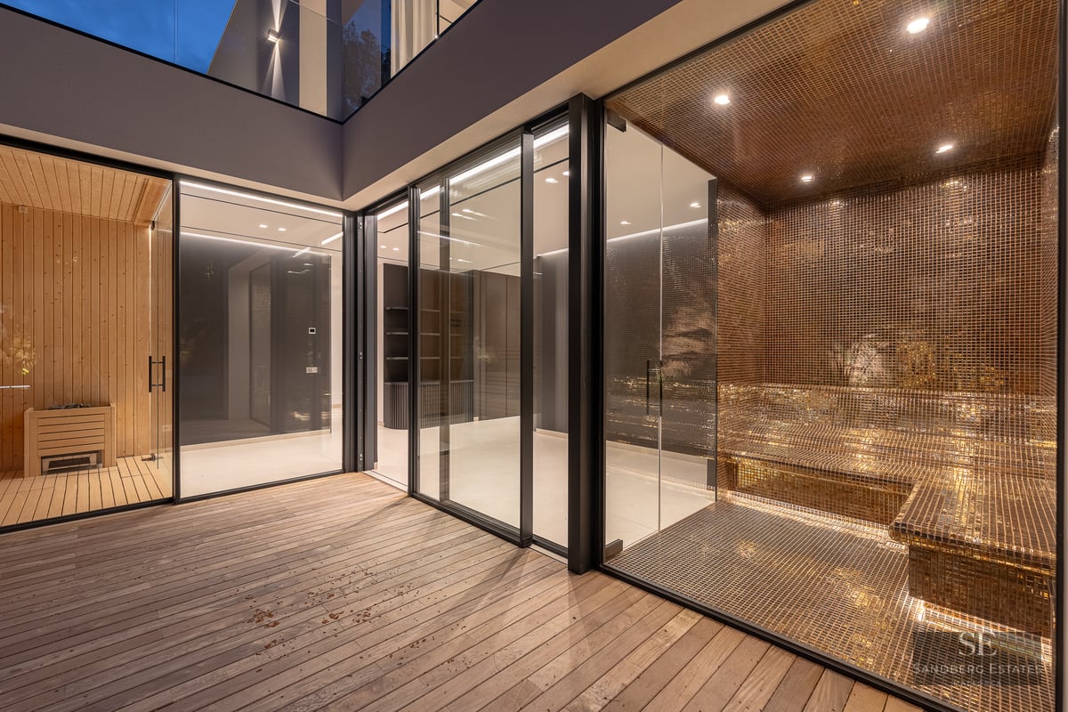 Modern spa area featuring a wooden sauna and gold mosaic steam room behind glass walls and a wooden deck.