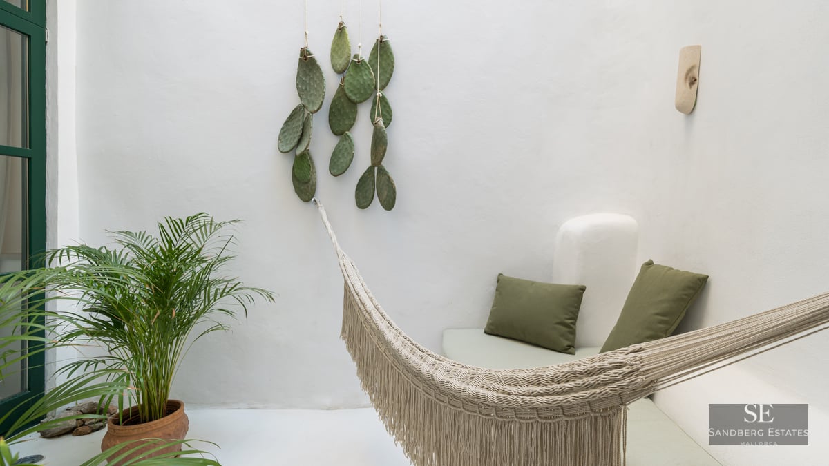 White minimalist terrace featuring a cream woven hammock, green cushions on a built-in bench, and a potted palm plant.