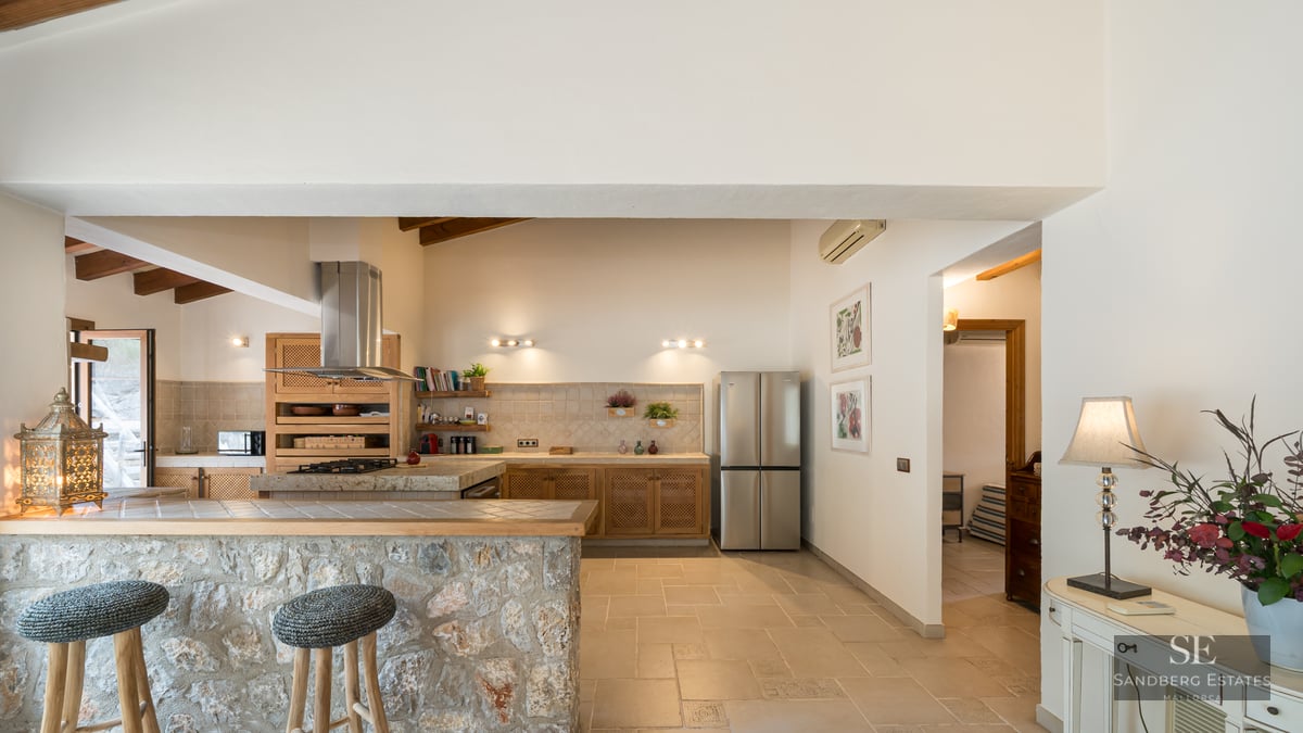 Spacious kitchen featuring a natural stone bar, stools, wooden ceiling beams, and stainless steel appliances.