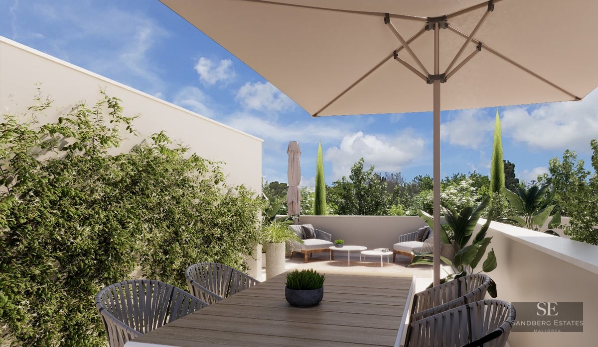 Bright outdoor terrace with a wooden dining table, large sun umbrella, lounge chairs, and lush green plants.