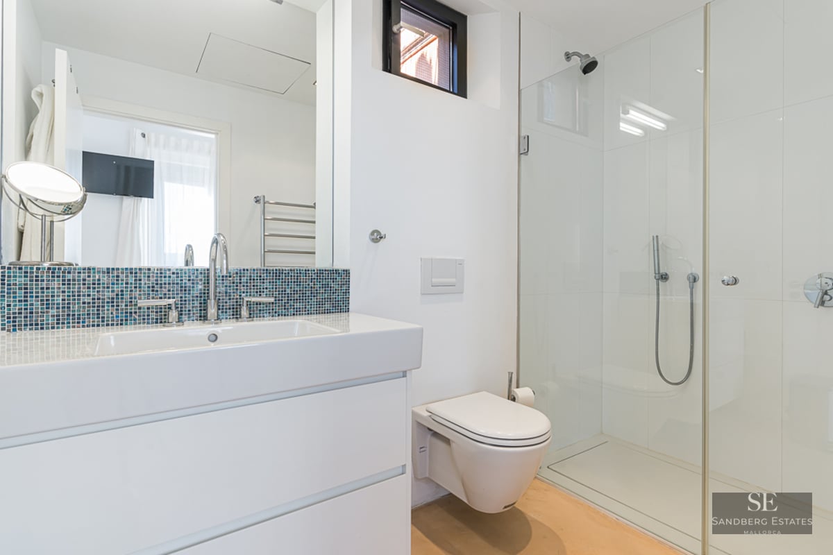 Contemporary bathroom featuring a white vanity, blue mosaic backsplash, wall-mounted toilet, and glass walk-in shower.