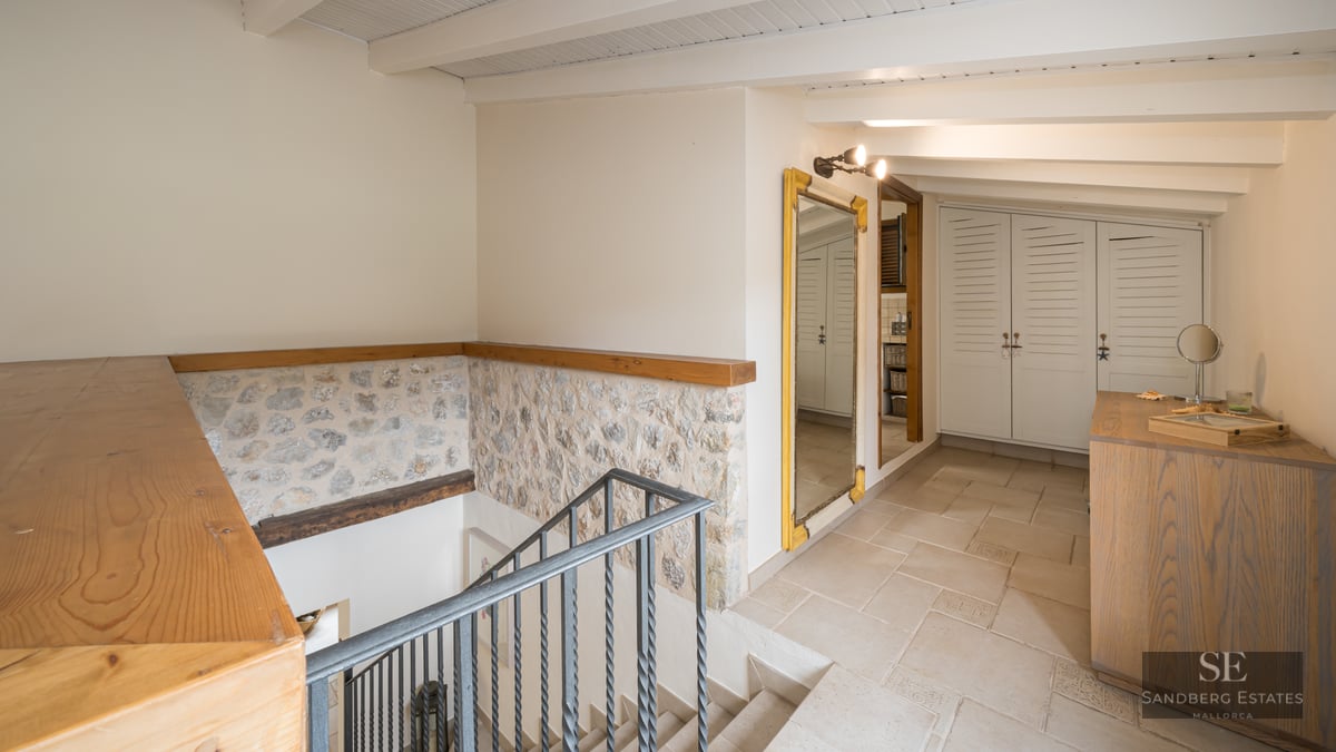 Interior landing featuring a wrought iron staircase, exposed stone walls, wooden ceiling beams, and white built-in wardrobes.