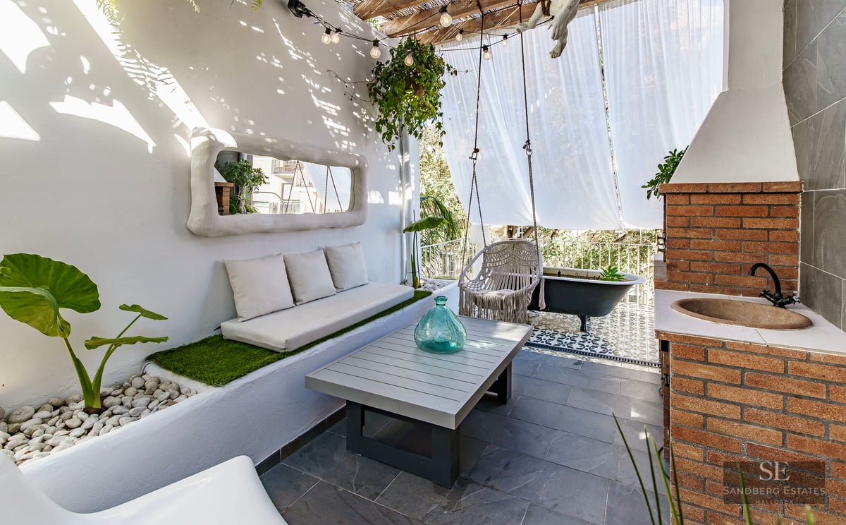 Sun-drenched white terrace with built-in sofa, macrame swing, brick outdoor sink, and a black clawfoot bathtub.