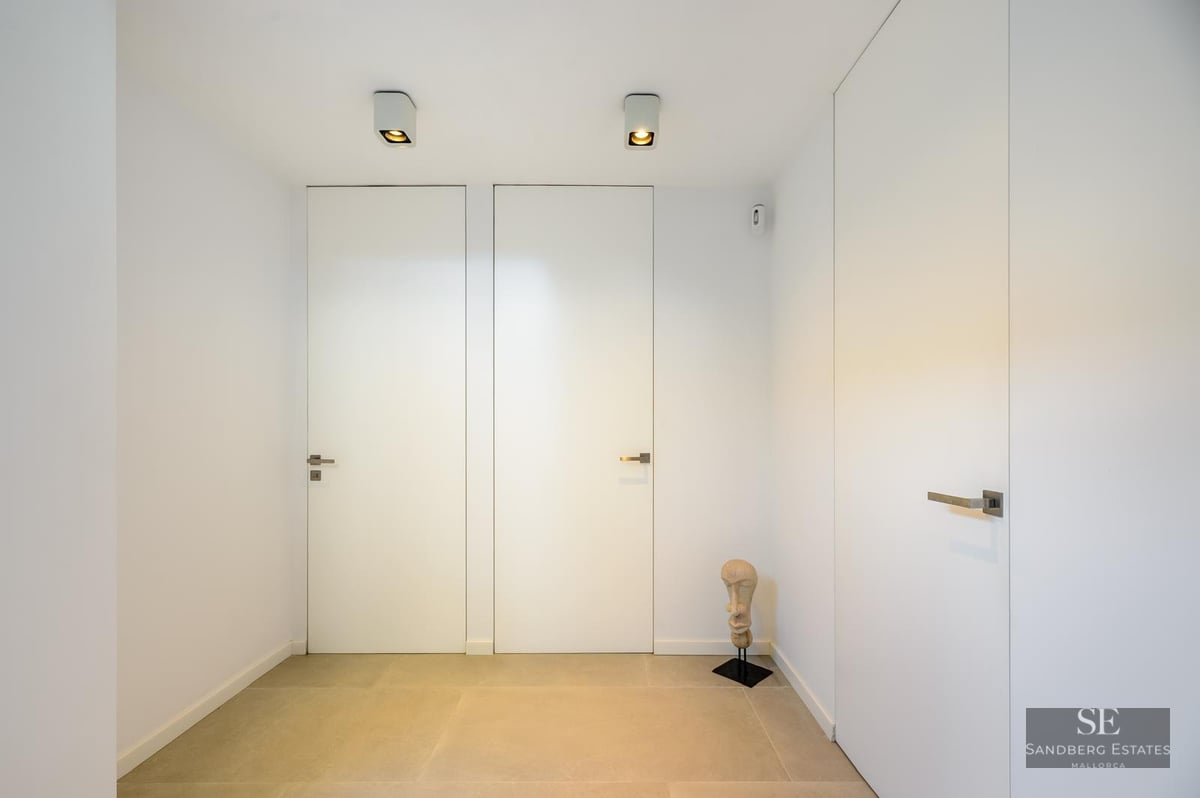 Minimalist hallway with flush white doors, light stone flooring, and a small decorative head sculpture.