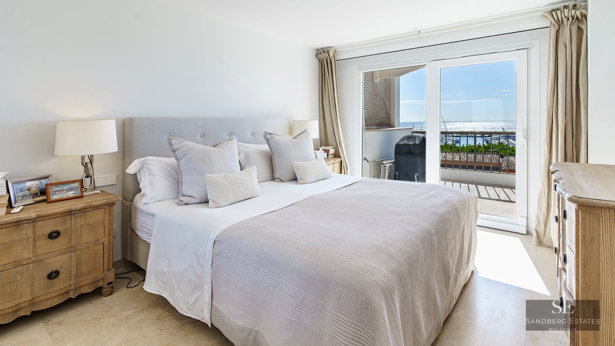 Bright bedroom featuring a large bed, wooden nightstands, and sliding glass doors with views of the sea and marina.