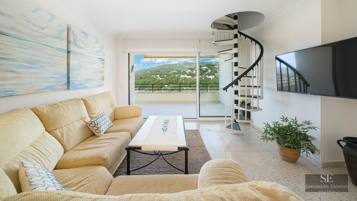 Bright living room featuring a cream sofa, black and white spiral staircase, and balcony with mountain views.
