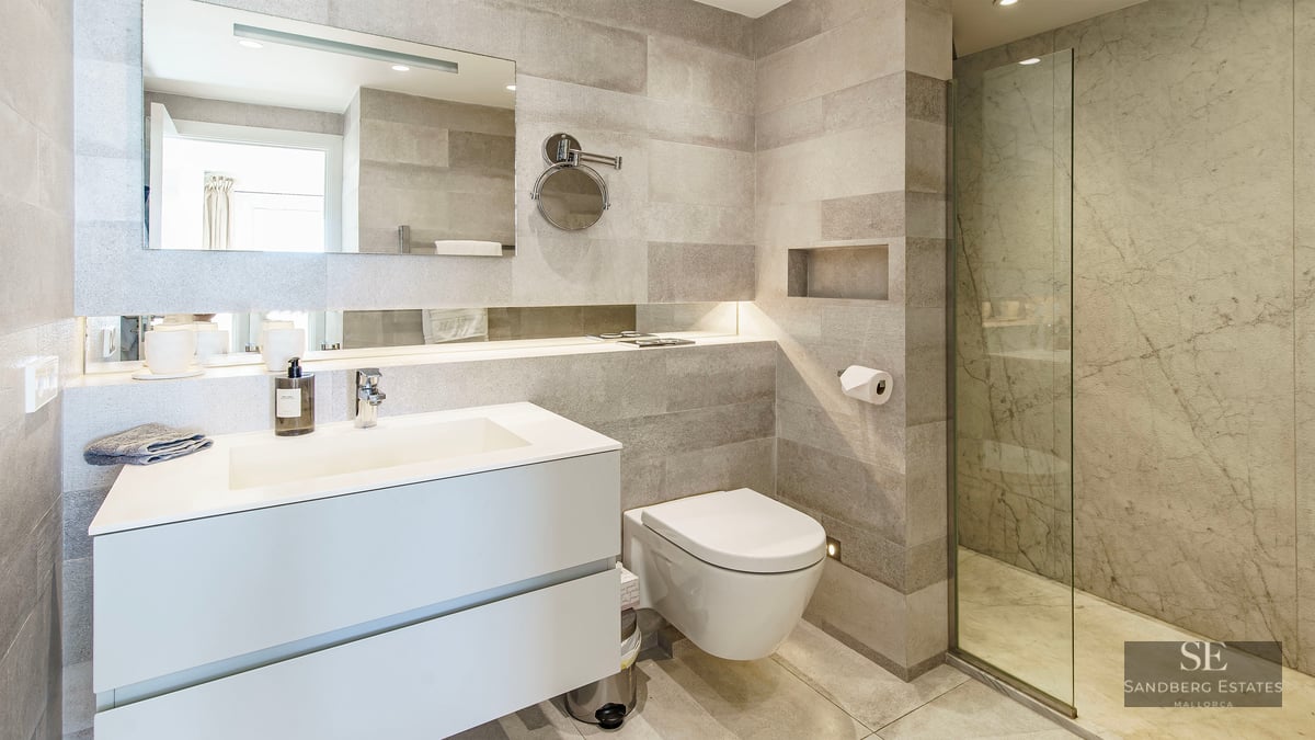 Minimalist bathroom featuring grey stone walls, white floating vanity, and a glass walk-in shower.