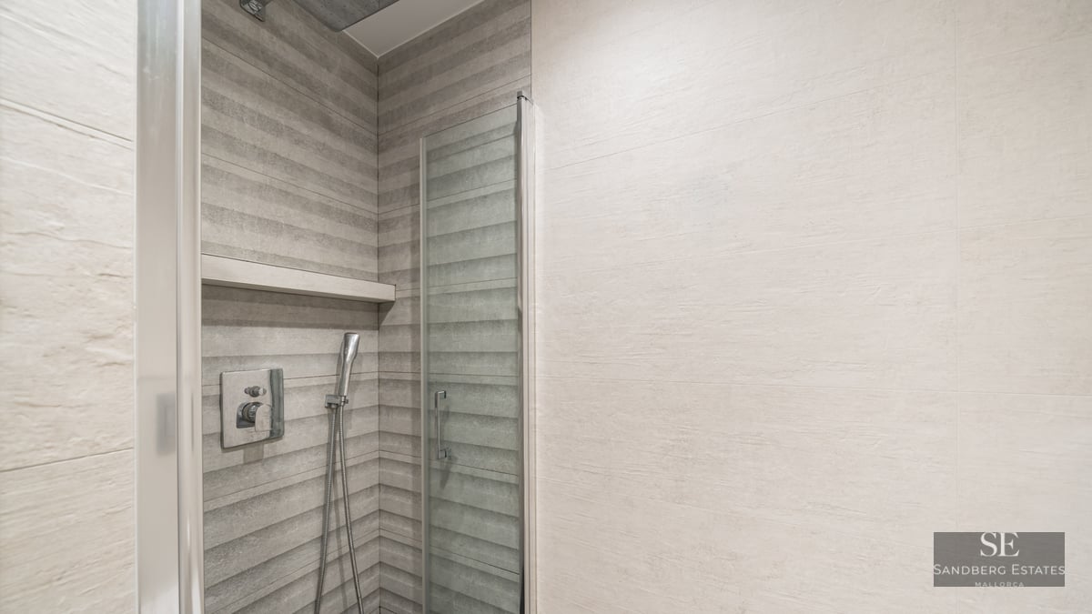 Douche moderne avec carrelage gris texturé, paroi en verre et robinetterie en chrome.