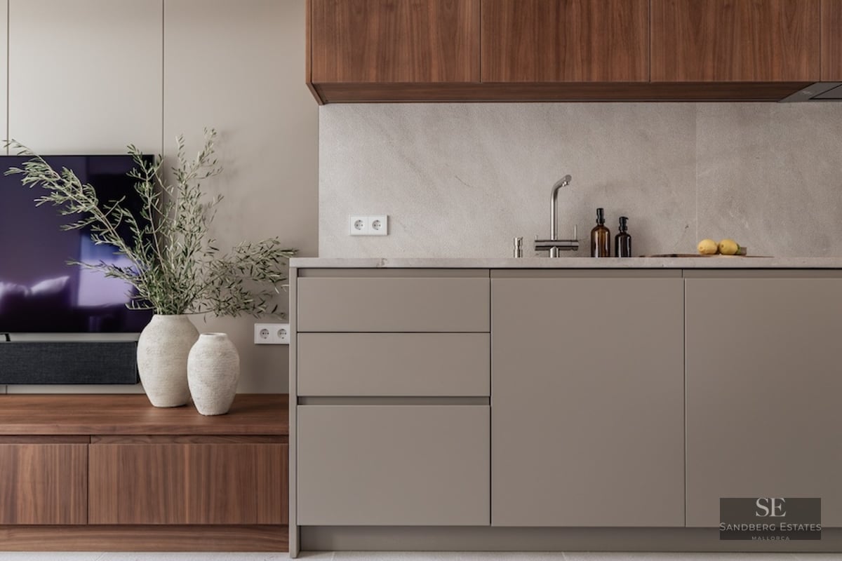 Modern kitchen with taupe cabinets, stone countertop, and walnut wood accents next to a TV unit.