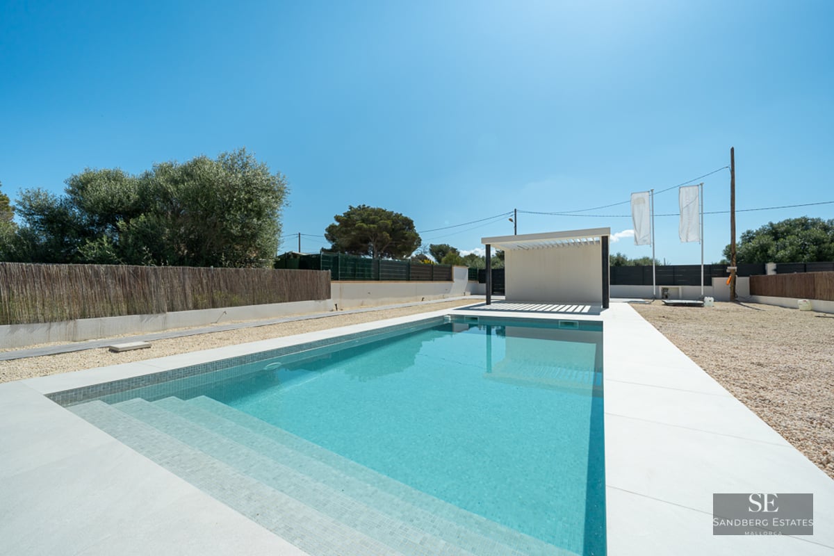 Rectangular turquoise pool with white tile border and a modern white pergola under a clear blue sky.