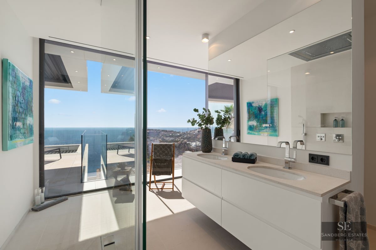 Modern bathroom featuring a double white vanity and floor-to-ceiling windows overlooking the Mediterranean sea and coastline.