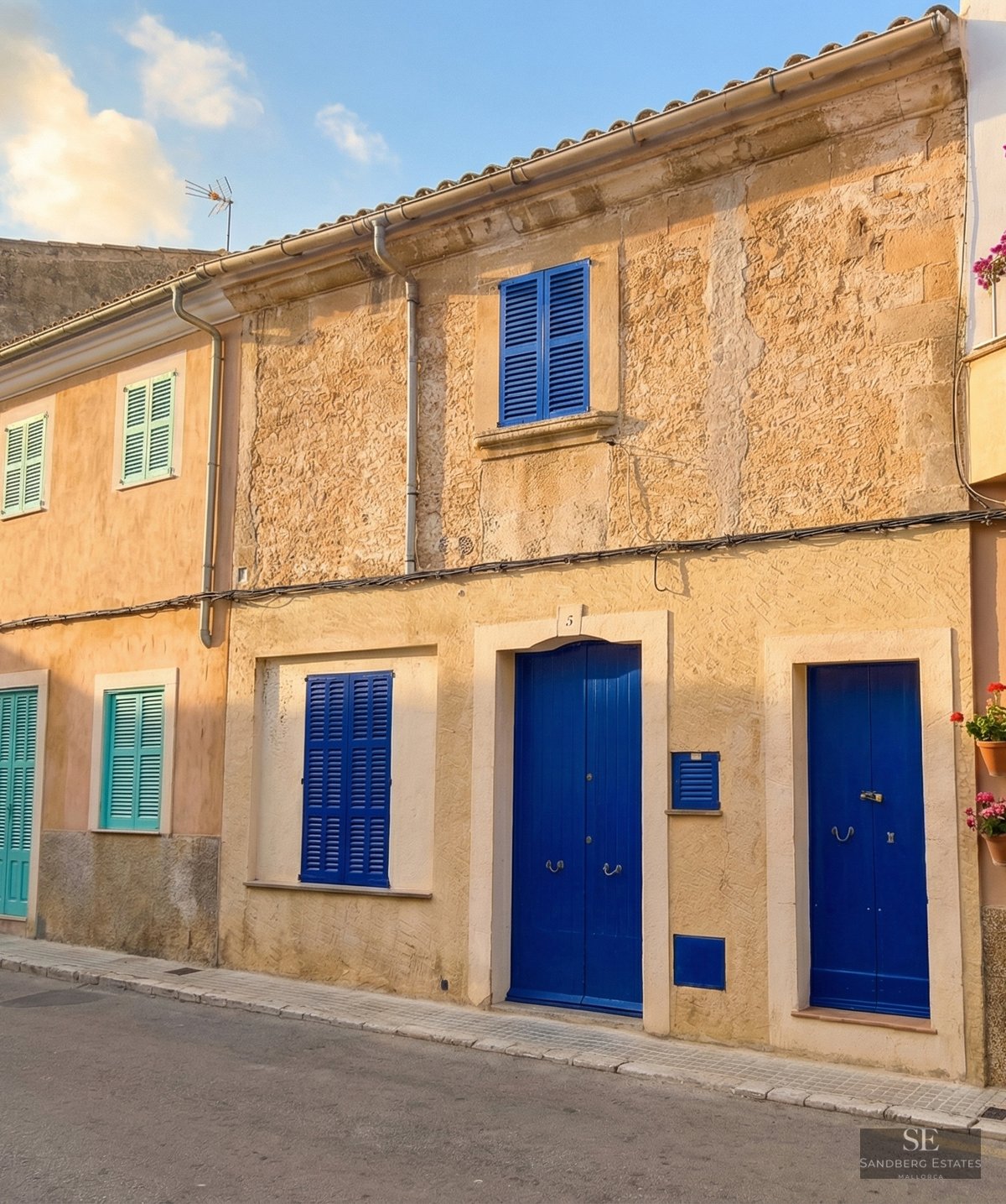 Ochre stone facade featuring vibrant blue wooden doors and shutters on a quiet street.