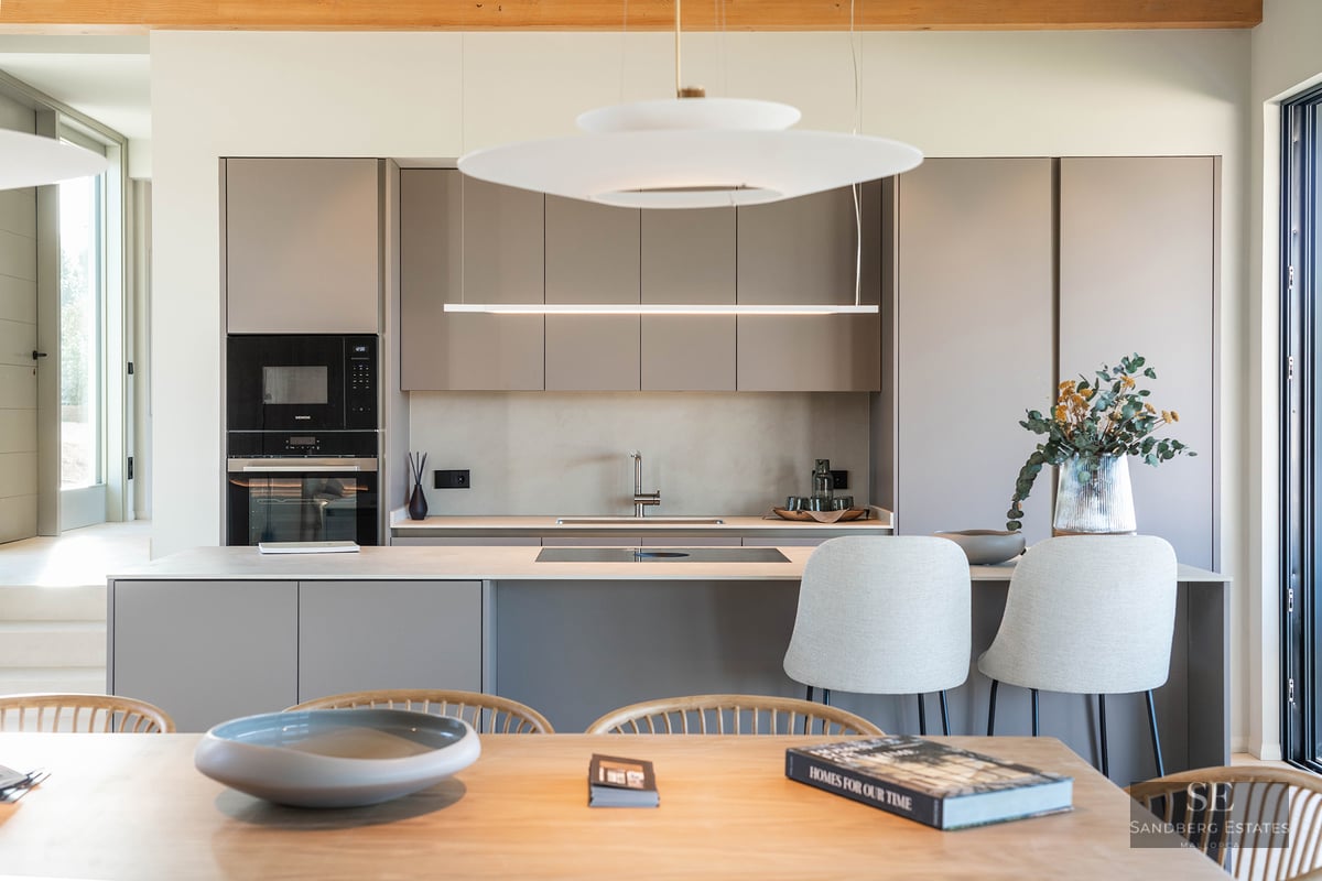 A contemporary kitchen featuring taupe handleless cabinets, a central island with stools, and elegant pendant lights.