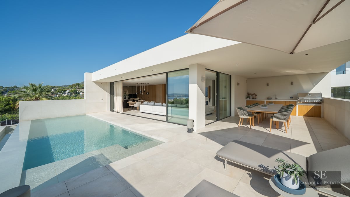 Modern villa terrace with infinity pool, sun loungers, outdoor dining area, and seamless indoor-outdoor living space.