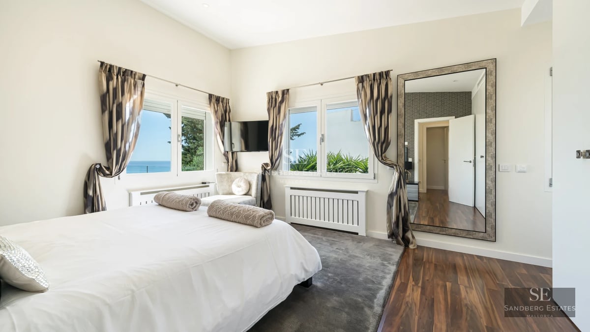 Spacious living room with floor-to-ceiling windows overlooking the sea. Modern sofa, light rug, minimalist details. Abundant natural light.