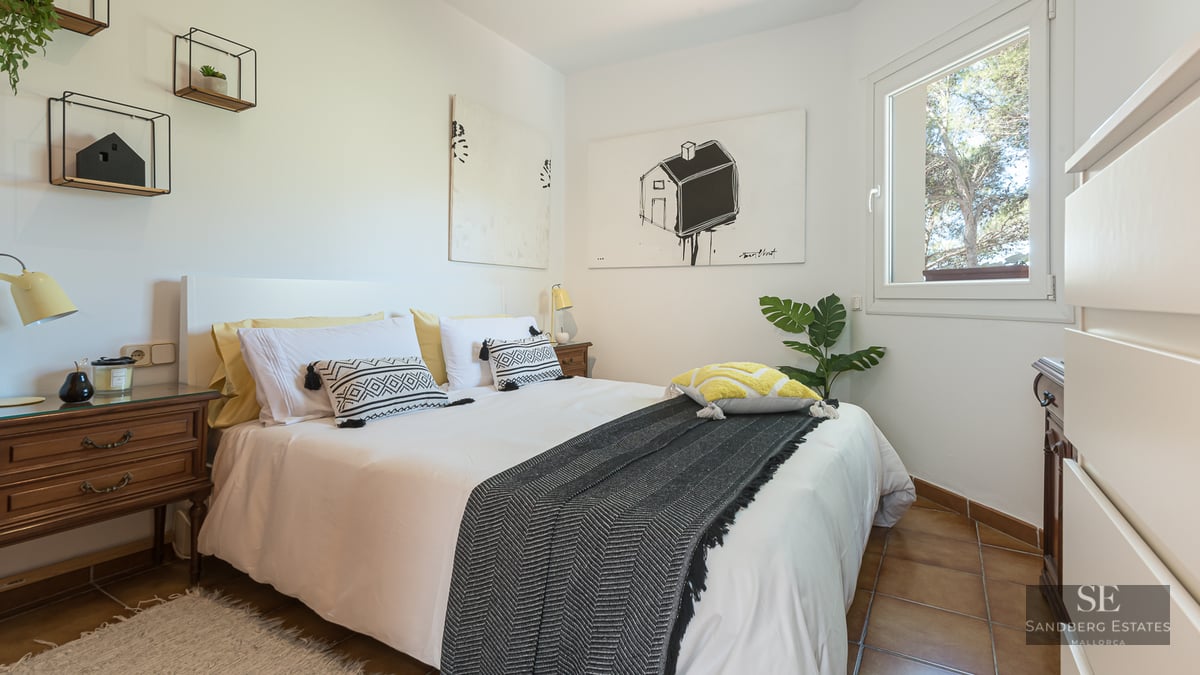 Modern bedroom with a white bed, patterned pillows, wooden nightstands, and tile flooring under natural light.