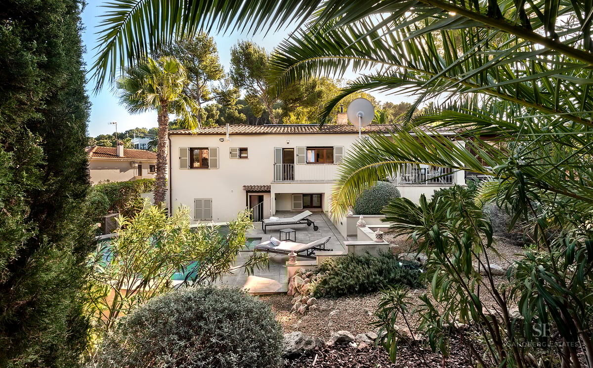 Two-story villa with a private swimming pool, sun loungers, and lush Mediterranean greenery under a clear sky.