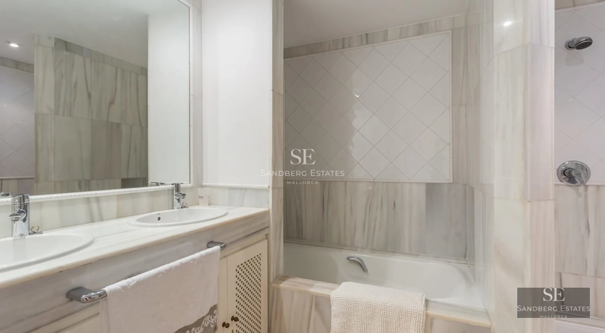 View of a luxurious pool with sun loungers, lush greenery, and a modern house with large windows in the background.