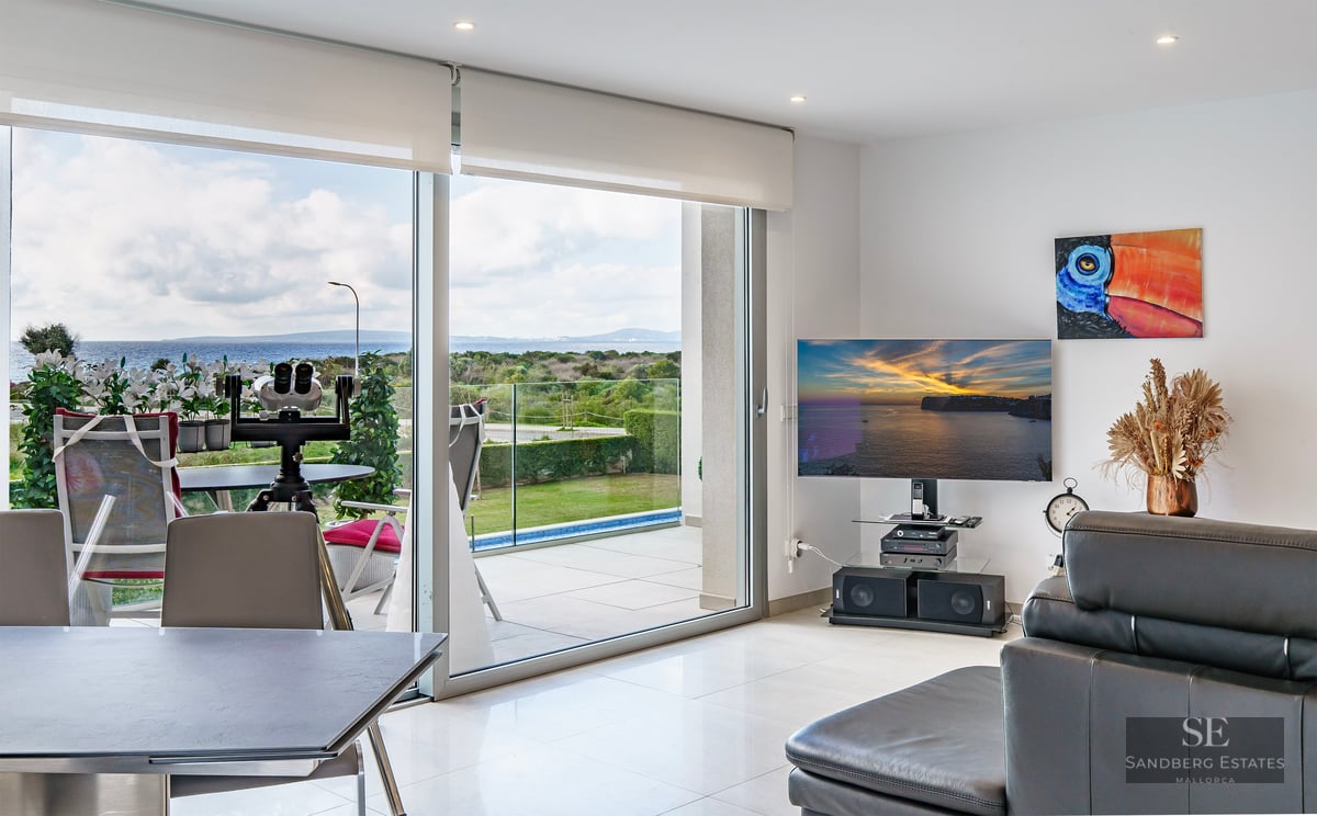 Bright living room with large glass doors opening to a terrace with sea views, featuring a TV and leather sofa.