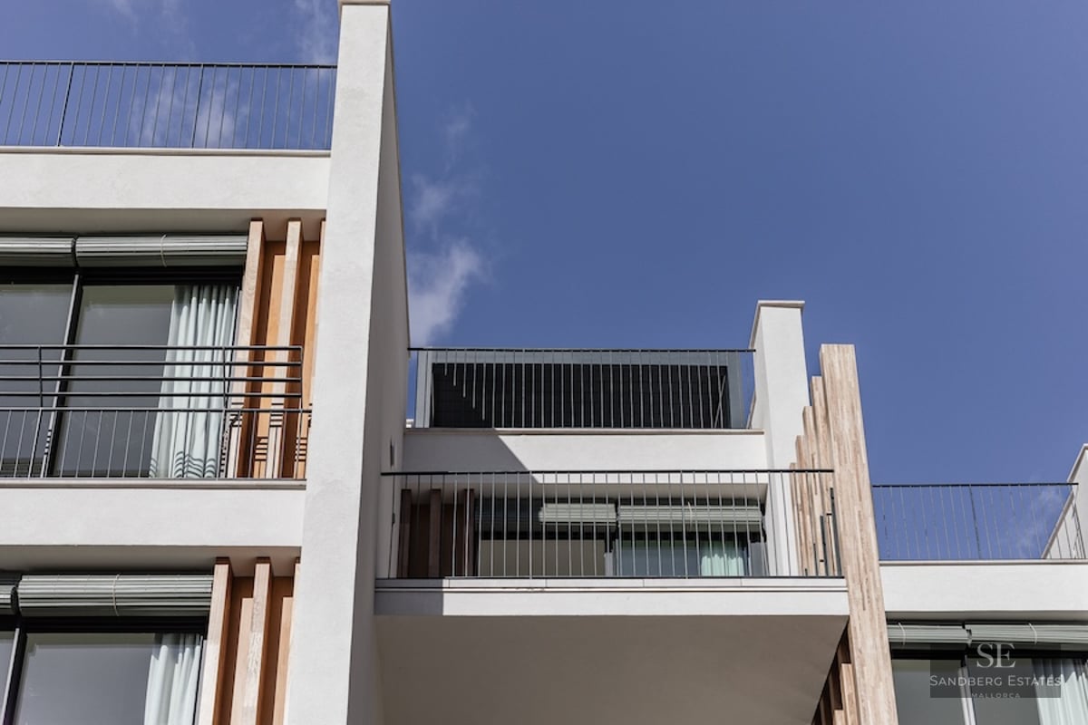 Low angle view of a modern white building with metal railings, wooden slats, and large glass windows under a blue sky.