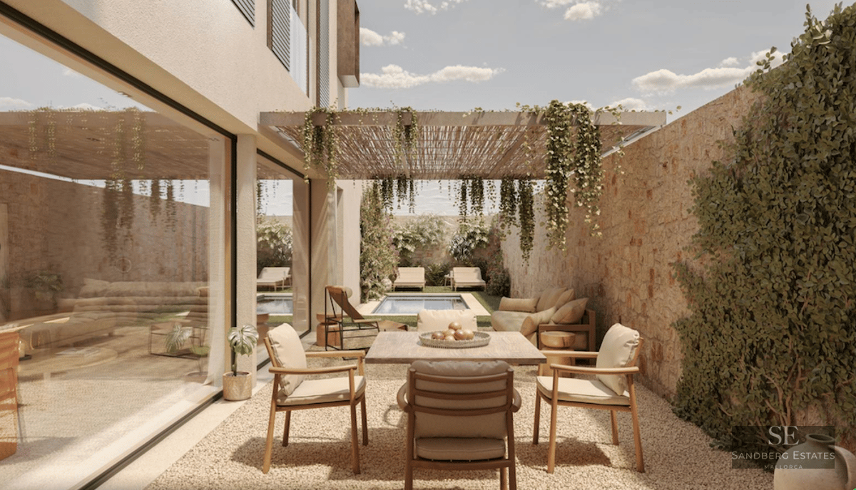Modern outdoor terrace with a wooden dining table, a stone wall, a pergola with plants, and a pool in the background.