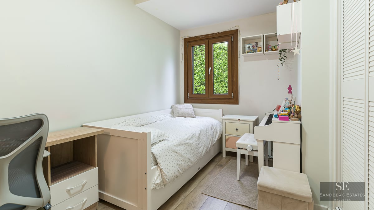 Bright bedroom with a single white bed, a desk, a white digital piano, and a window showing green foliage.