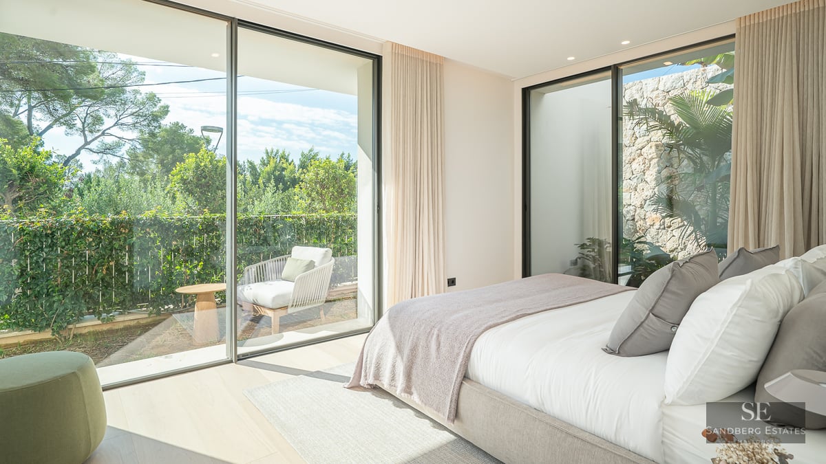 Bright master bedroom featuring floor-to-ceiling glass doors opening onto a private terrace with lush greenery.