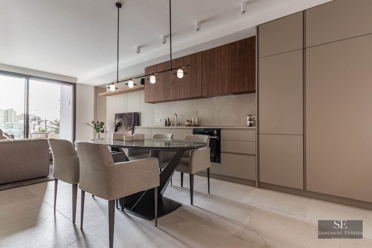 Modern dining area with an oval dark marble table, beige chairs, and a minimalist kitchen with wood accents.