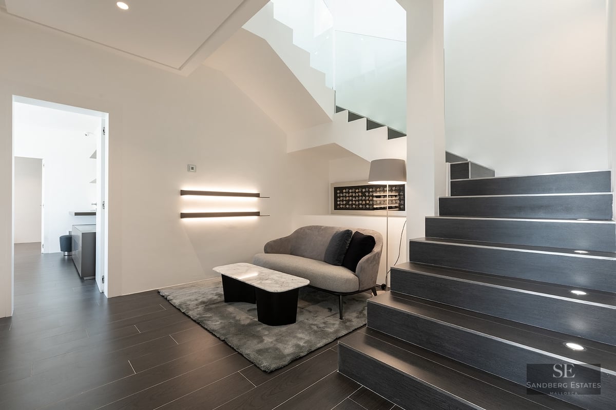 Modern interior featuring dark stairs with integrated LED lighting, a gray sofa, and a marble coffee table.