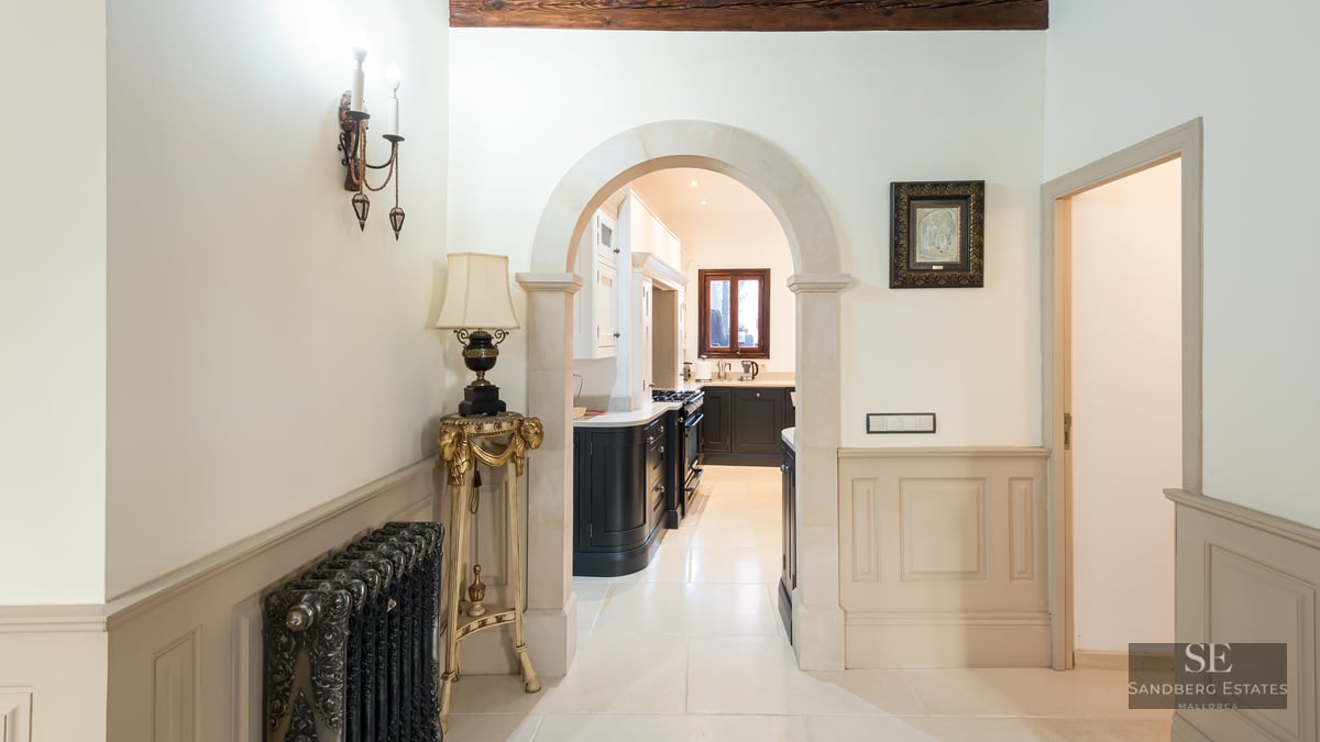 Elegant hallway with a stone archway leading to a kitchen, featuring an ornate radiator and classic wainscoting.