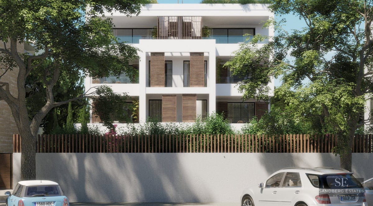 White four-story modern building with wooden shutters and glass balconies framed by large green trees.