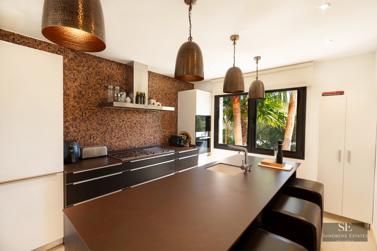 Modern kitchen featuring a large brown island, copper mosaic backsplash, and four bronze hammered pendant lamps.