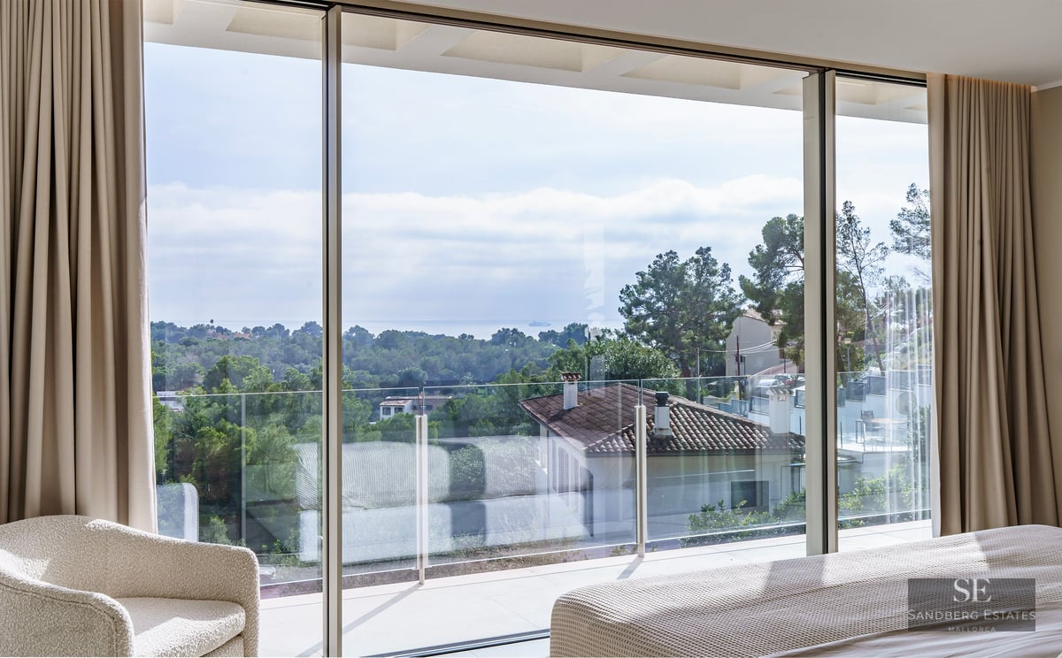 Luxury bedroom with floor-to-ceiling windows overlooking a Mediterranean landscape and the sea.